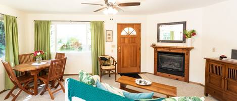 A cozy living room with a wooden dining table, a sofa, a fireplace, and a ceiling fan.