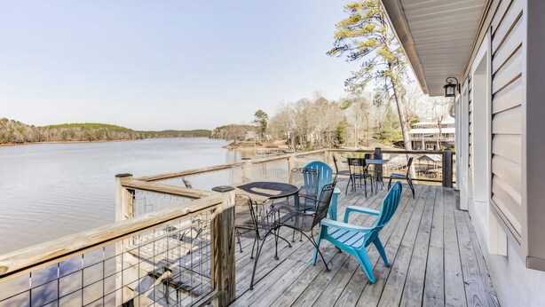A wooden deck with outdoor seating, overlooking a calm body of water.