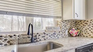 A kitchen with a marble countertop, a sink, and a window with blinds. A sign on the wall reads "Lake Rulez."
