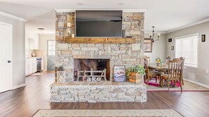 A living room with a stone fireplace, a flat-screen TV, and a dining area with wooden furniture.