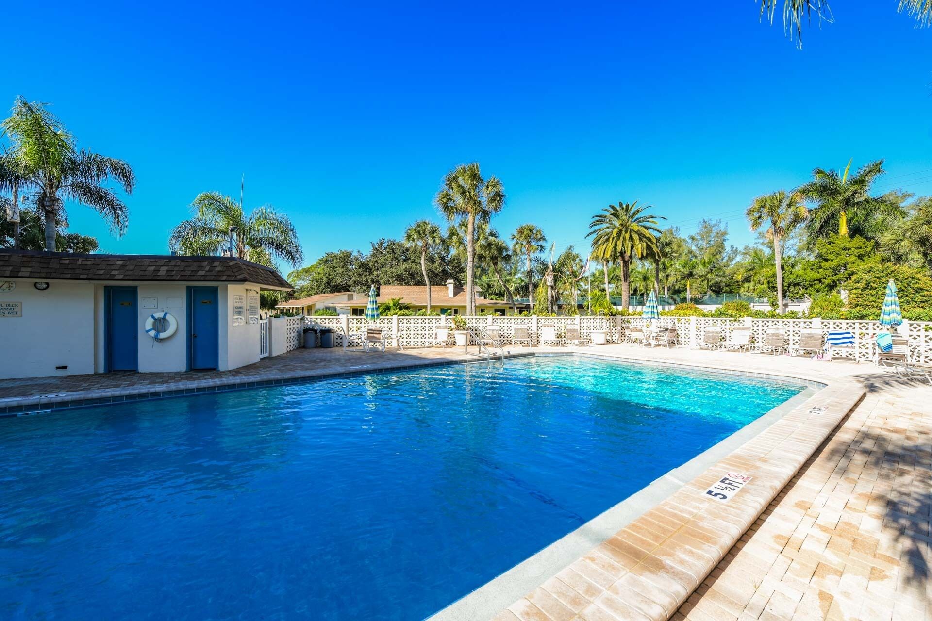 Una piscina con valla blanca, palmeras y un edificio con puertas azules.