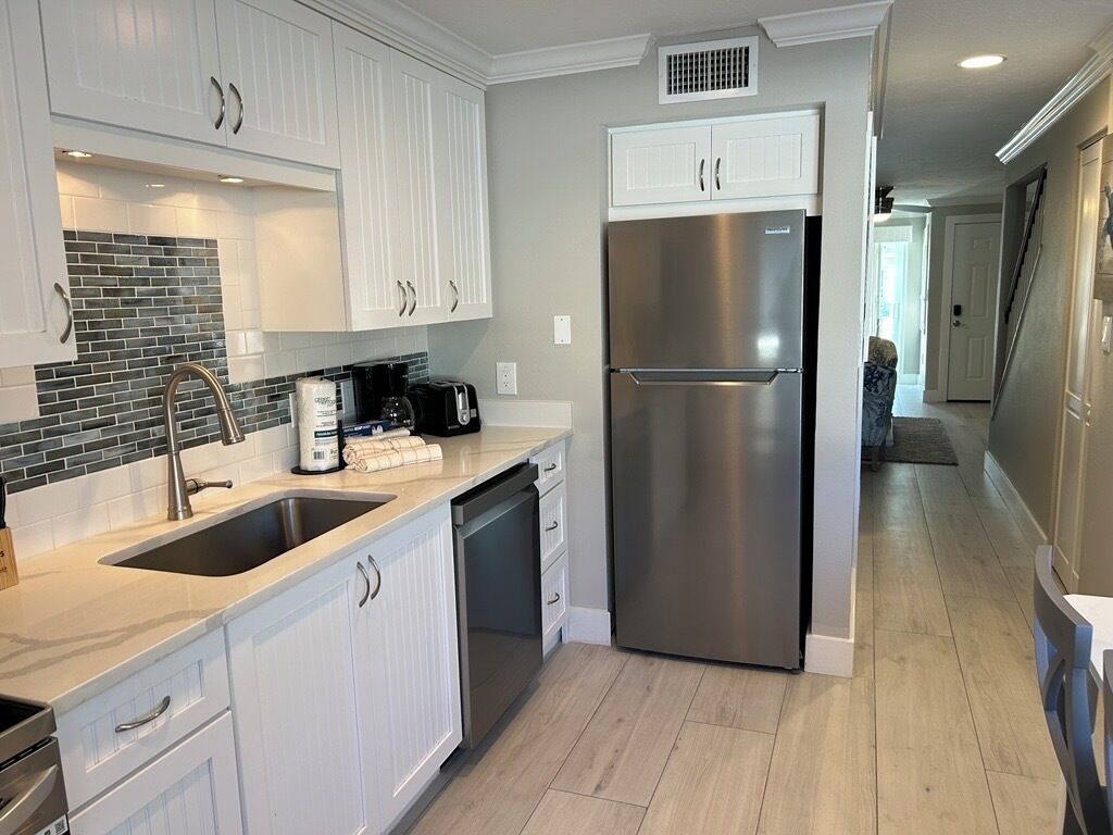 A modern kitchen with white cabinets, a stainless steel refrigerator, and a black tiled backsplash.