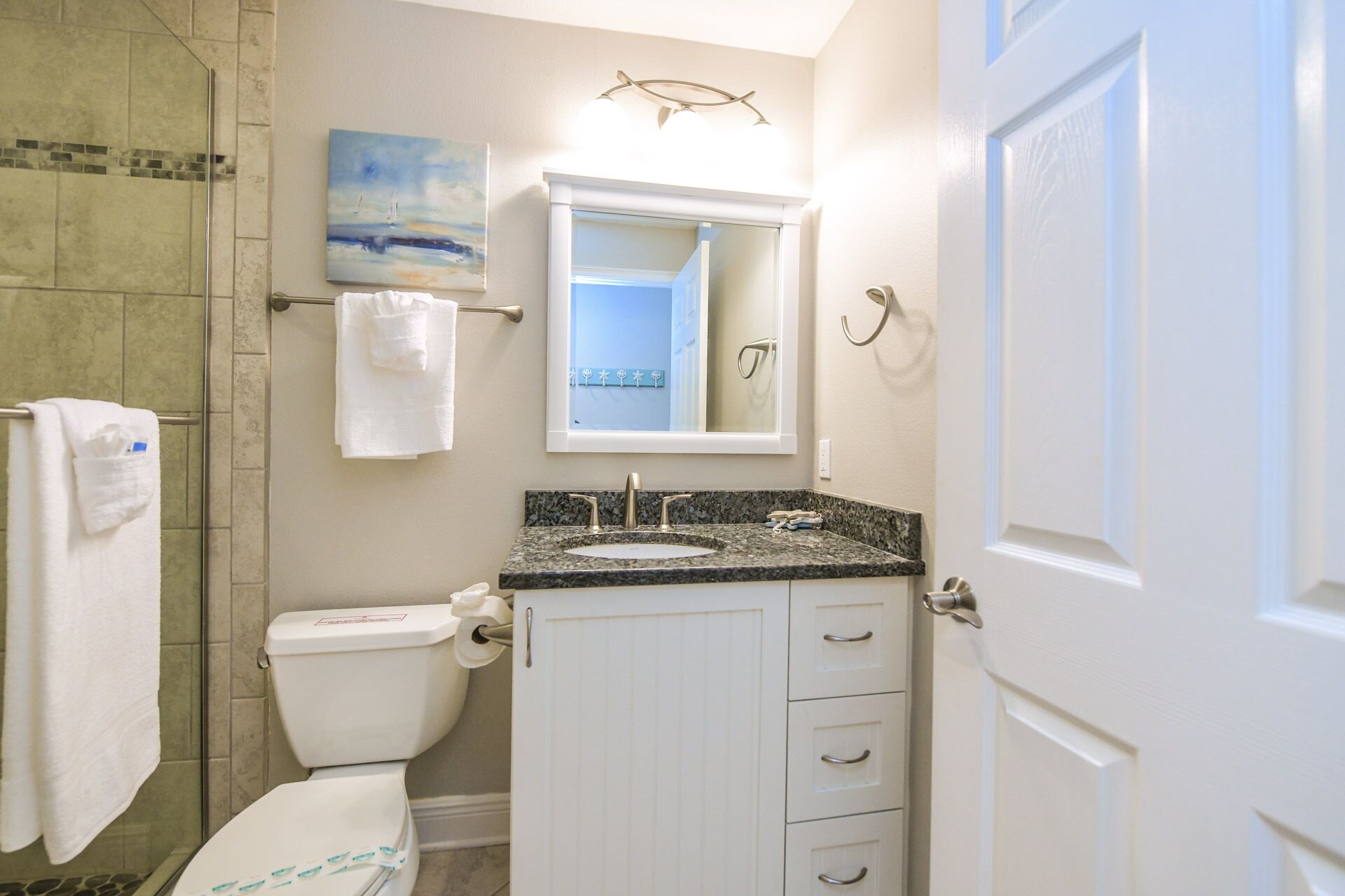 A bathroom with a toilet, sink, and shower. There is a towel rack with towels, a mirror above the sink, and a door to the right.