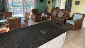 A spacious living area with a brown leather sofa, wicker chairs, a glass coffee table, and a kitchen island with a black countertop. - DUPLEX IN DUCK KEY, 2 Bedroom/2 Bath, W/Private 90' Dock,  Trailer Storage (Duck Key)