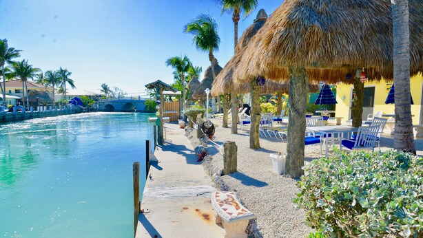 A poolside area with a concrete deck, lounge chairs, and thatched umbrellas. - DUPLEX IN DUCK KEY, 2 Bedroom/2 Bath, W/Private 90' Dock,  Trailer Storage (Duck Key)