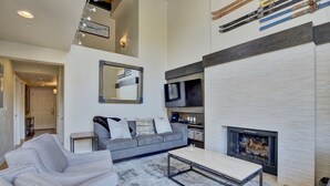 A modern living room with a fireplace, grey sofas, a coffee table, and a mounted TV.