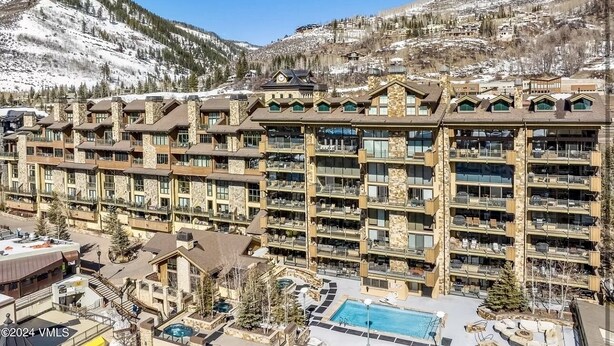 A multi-story hotel with a pool area, ski slopes in the background, and a mountainous landscape.