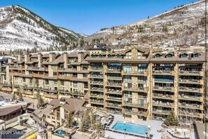Um hotel com vários andares, área de piscina, encostas de esqui ao fundo e paisagem montanhosa.