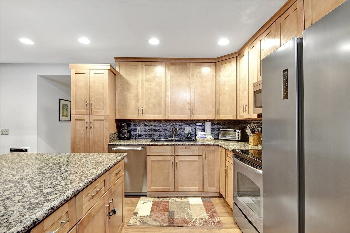 A modern kitchen with wooden cabinets, granite countertops, a stainless steel refrigerator, and a built-in oven.