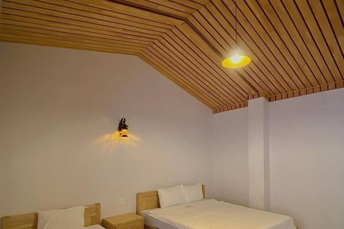 A bedroom with two beds, a sloped wooden ceiling, and a wall-mounted light fixture.