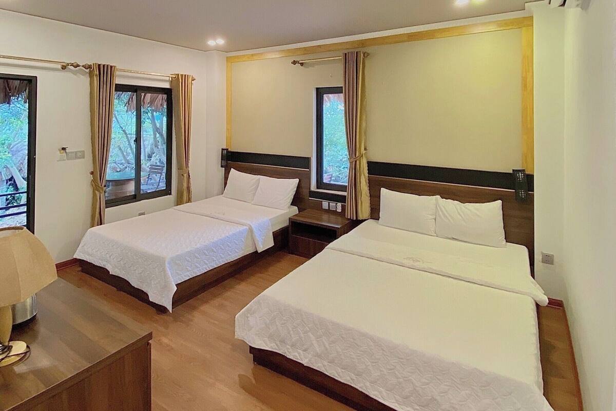 A hotel room with two single beds, a wooden desk, and a window with curtains.