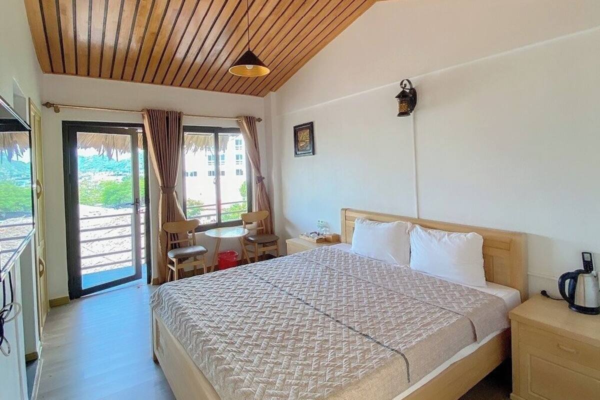 A bedroom with a large bed, wooden ceiling, and a view of the outdoors through a sliding door.