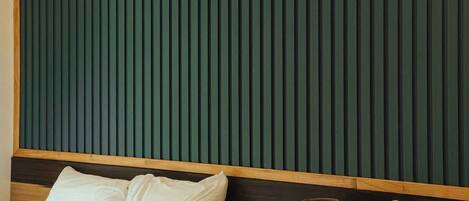 Habitación de hotel con dos camas, cabecero de madera, panel acústico verde y lámpara de noche.