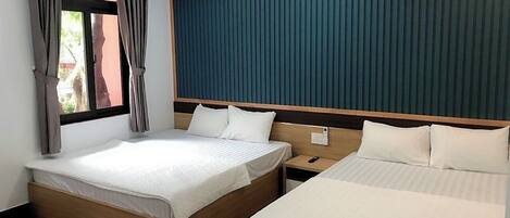 A hotel room with two beds, wooden headboards, a window with curtains, and a wooden floor.