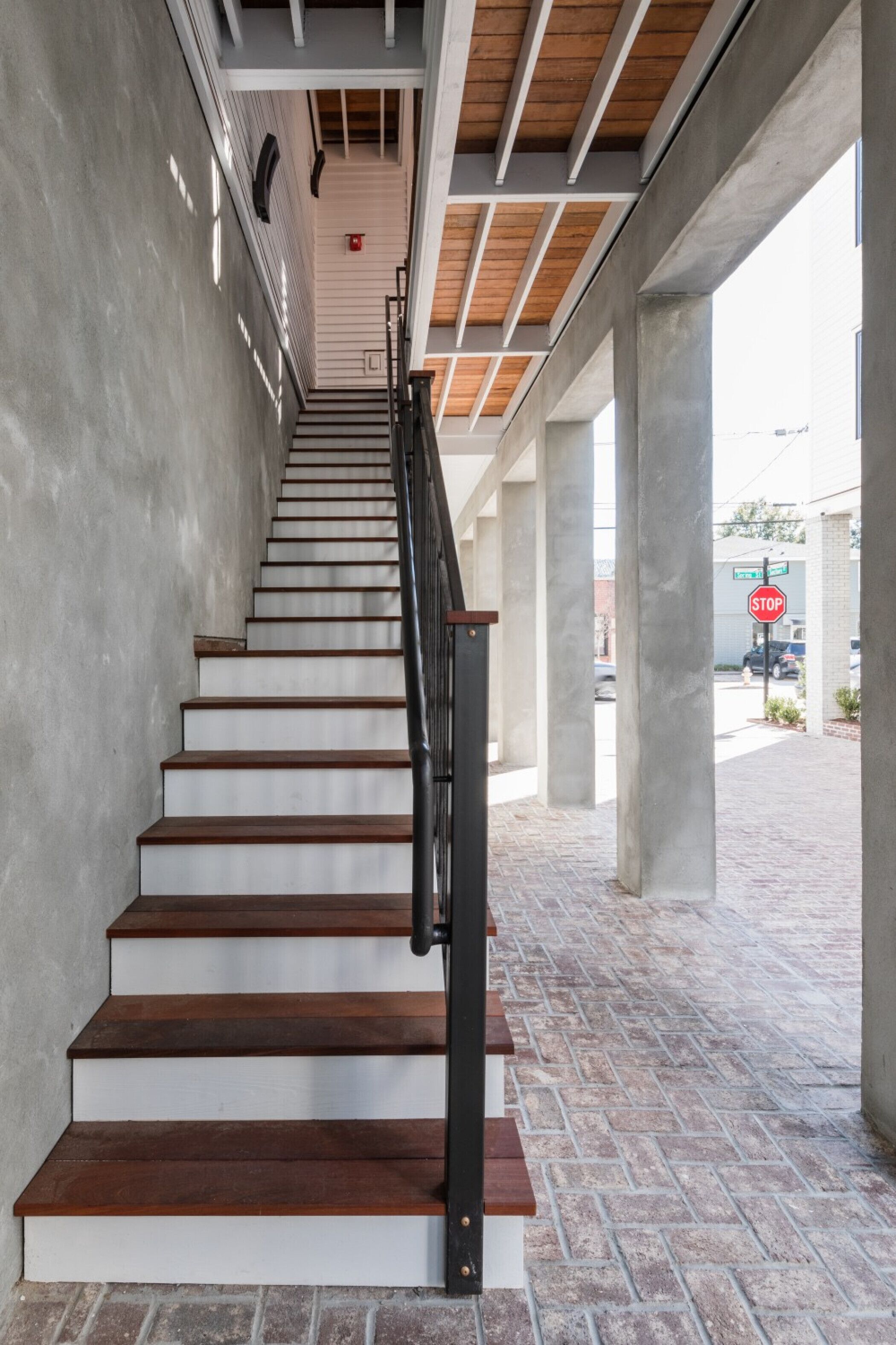A staircase with wooden steps and a metal railing, leading to an outdoor area with a brick floor and a stop sign in the background.