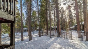 Une forêt enneigée avec un chalet en bois et une zone délimitée par une clôture.