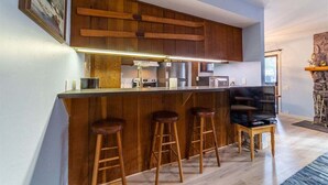 Une cuisine moderne avec des meubles en bois, un coin bar doté de tabourets et un mur d’accent en pierre.