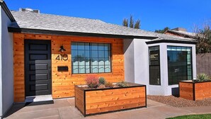 A modern house with a wooden facade, a black door, and a large window. - Stylish Retreat: Heated Pool w/ Jets, Putting Green & Outdoor Kitchen (Phoenix)