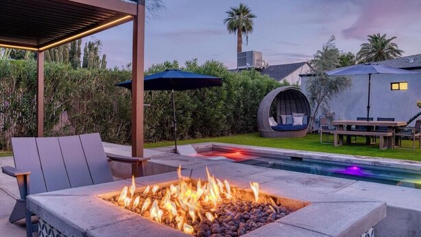 A fire pit with seating, a pool, and a covered area with a table and chairs. - Stylish Retreat: Heated Pool w/ Jets, Putting Green & Outdoor Kitchen (Phoenix)