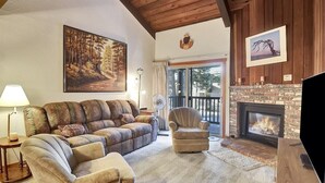 A cozy living room with a fireplace, a large painting of a forest, and a comfortable sofa. - Chamonix 40: Near Canyon Lodge (Mammoth Lakes)