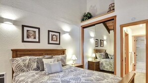 A bedroom with a large bed, wooden headboard, bedside tables with lamps, framed pictures on the wall, and a mirror reflecting the room. - Chamonix 40: Near Canyon Lodge (Mammoth Lakes)