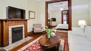 A living room with a fireplace, a television, a sofa, and a bed in the background. - Large Shotgun Double In Perfect Uptown Location  (New Orleans)