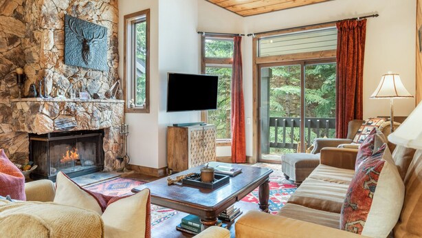 A stone fireplace, a flat-screen TV, a sofa, and a window with curtains. - Ridgepoint 202 | Updated 3BR+Loft Ski-Way Townhome (Avon)