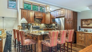 A kitchen with wooden cabinets, a stainless steel refrigerator, and a marble countertop. - Ridgepoint 202 | Updated 3BR+Loft Ski-Way Townhome (Avon)