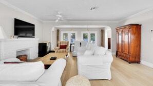 A living room with a white fireplace, a flat-screen TV, a white sofa, a wooden coffee table, and a large wooden cabinet. - ON HYPOLUXO ISLAND, Incredible Property  - Walk to Beach (Lantana)