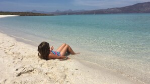 A person lying on a sandy beach with clear turquoise water and mountains in the background. - Beautiful 2 Bed, 2 Bath Casa Steps From The Beach & Pools In Loreto Bay (Loreto)