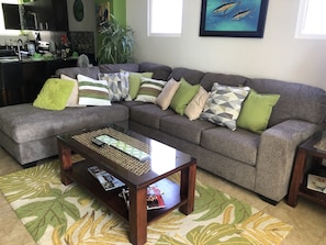 Una sala de estar con un sofá seccional gris, una mesa de centro de madera y un tapete estampado.
