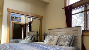 A bedroom with a large bed, a nightstand, a mirror, and a window with curtains.