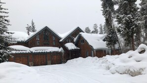 A large wooden cabin with a steep roof, surrounded by snow-covered trees.