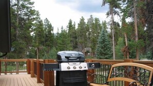 A deck with a grill, a bench, and a view of a forest.