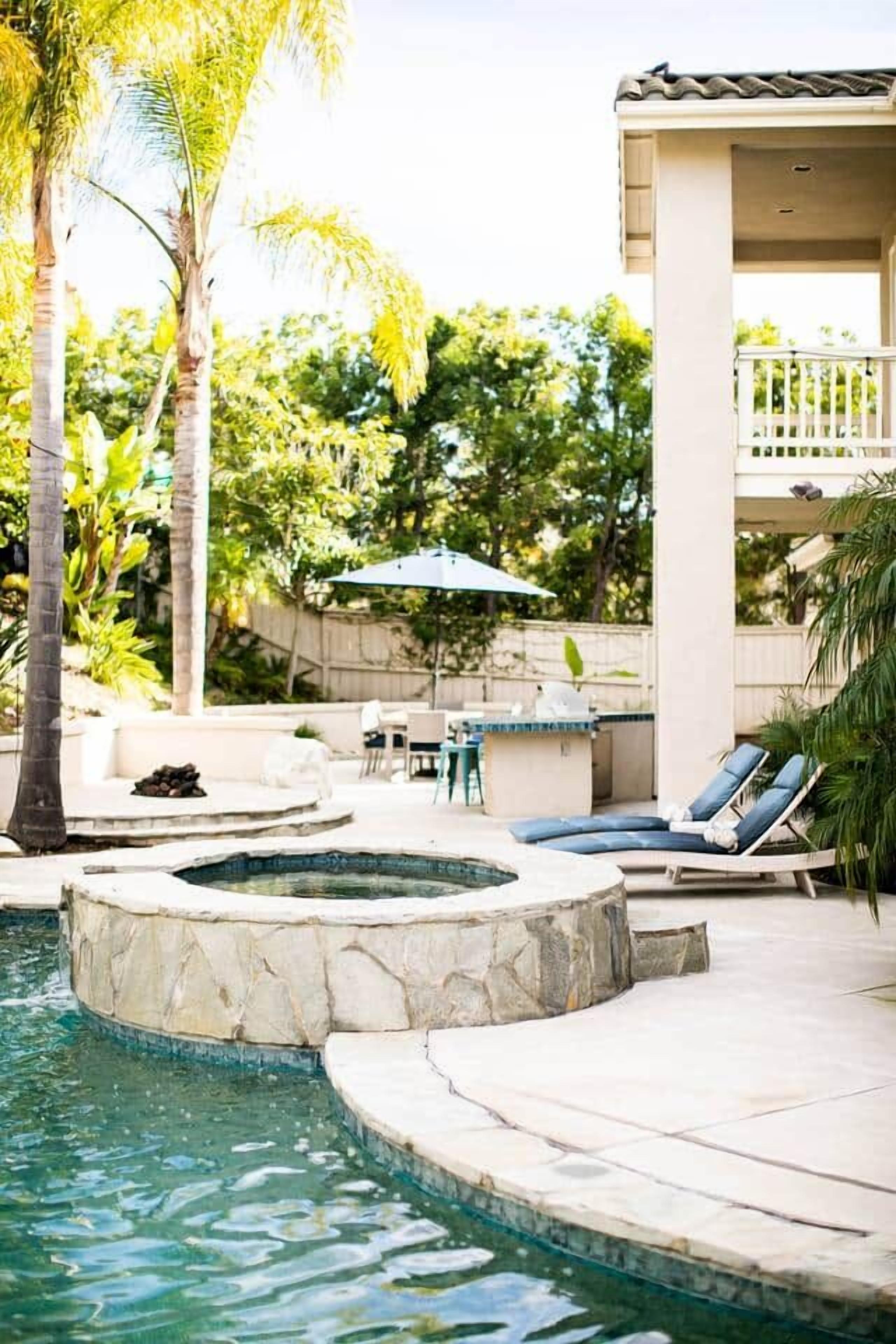 A pool area with a hot tub, lounge chairs, and a covered patio.