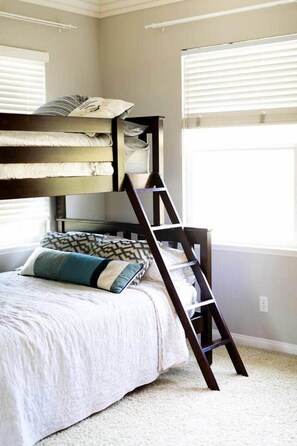 Una cama litera con escalera, una ventana con persianas y una almohada estampada en la cama.