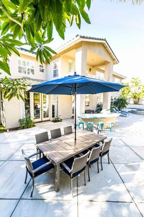 Un patio al aire libre con mesa y sillas, una sombrilla azul y una piscina al fondo.
