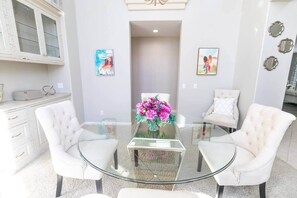 Una sala de estar moderna con una mesa de centro de vidrio, sillones tapizados en blanco y obras de arte en las paredes.
