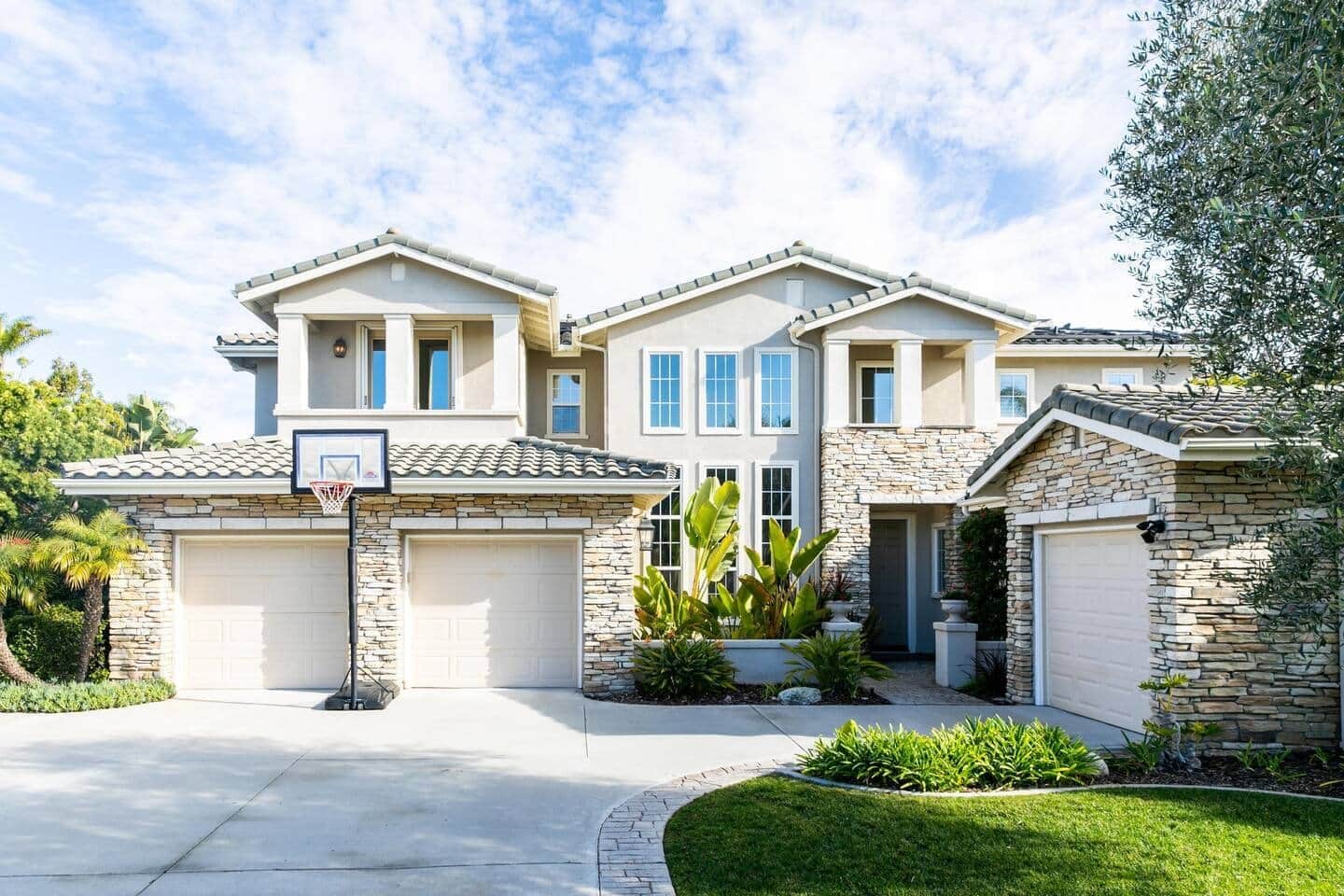 Une maison à deux étages avec une façade en pierre, un garage et un panier de basketball.