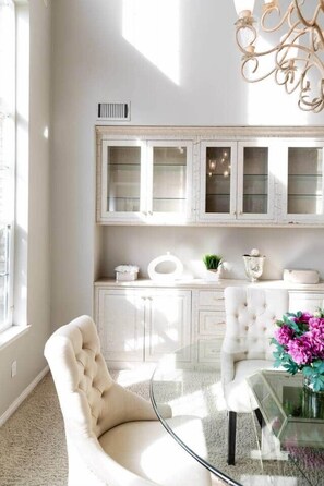 A room with a glass coffee table, a tufted armchair, and a white cabinet with glass doors.