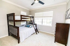 Un dormitorio con una cama litera, un aparador y un ventilador de techo.