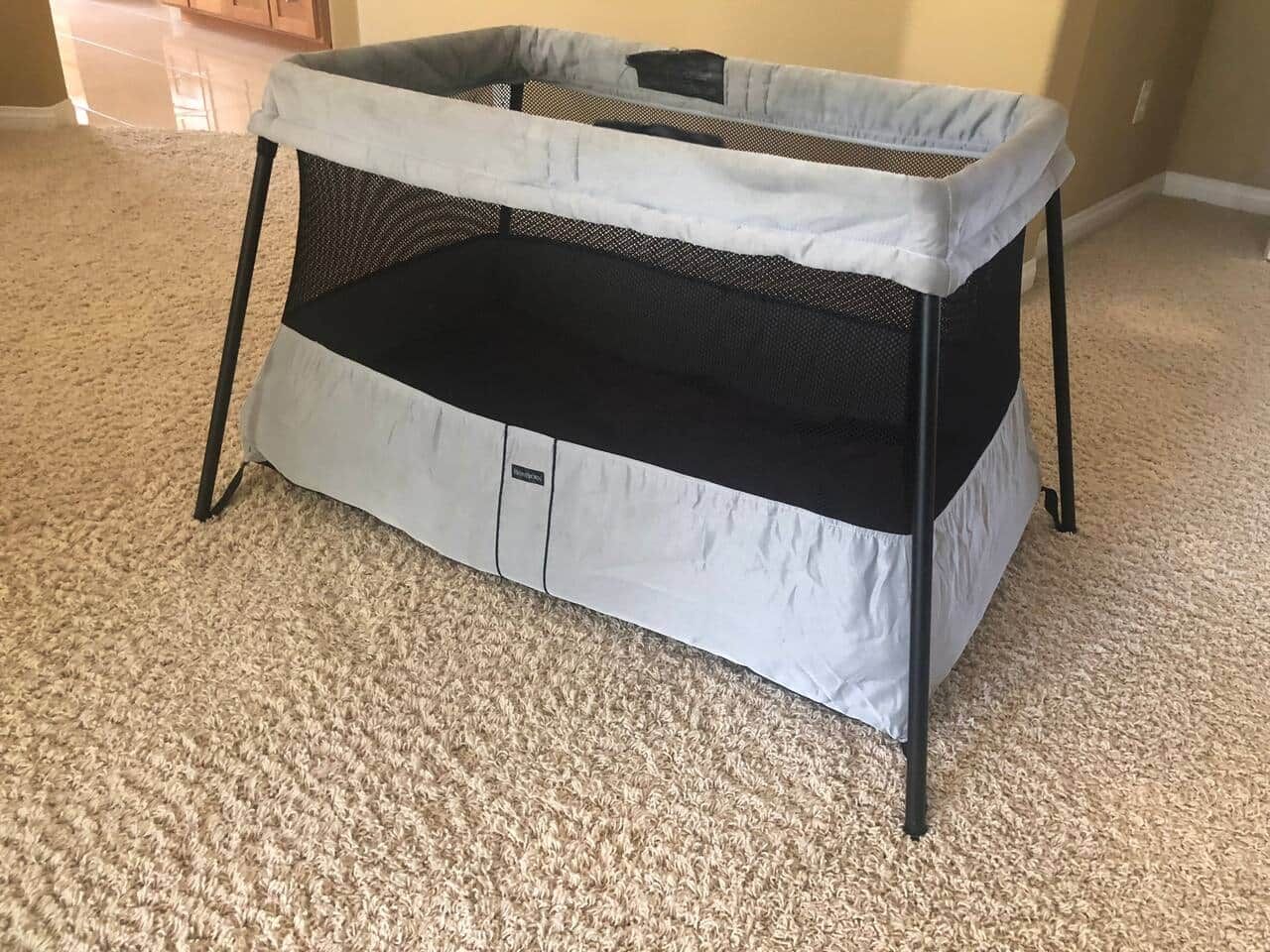 Un berceau portable doté d’un dessus en tissu ajouré et d’un fond rembourré, placé sur un sol recouvert d’une moquette.