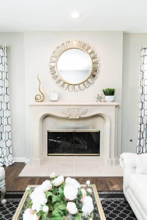 A living room with a fireplace, a round mirror, and a white sofa.
