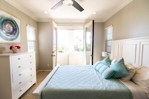 A bedroom with a bed, dresser, ceiling fan, and a view through an open door.