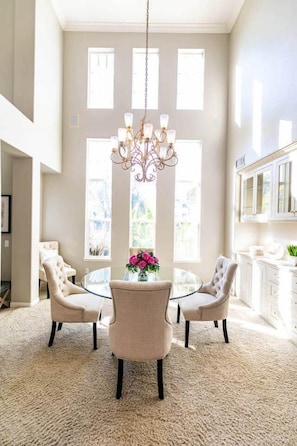 A dining area with a round table, four chairs, a chandelier, and a vase with flowers.