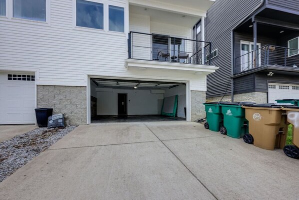 Un immeuble résidentiel de deux étages doté d’une entrée de garage, d’un balcon et de deux poubelles.