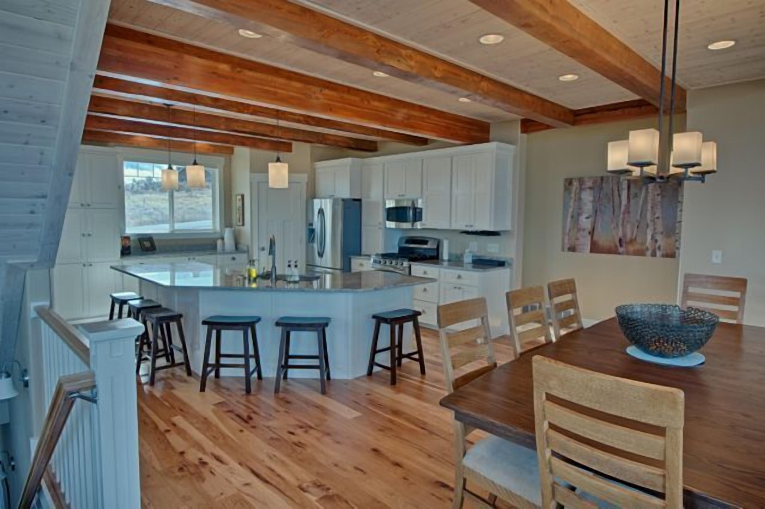 A modern kitchen with wooden beams, white cabinets, and a central island with stools.