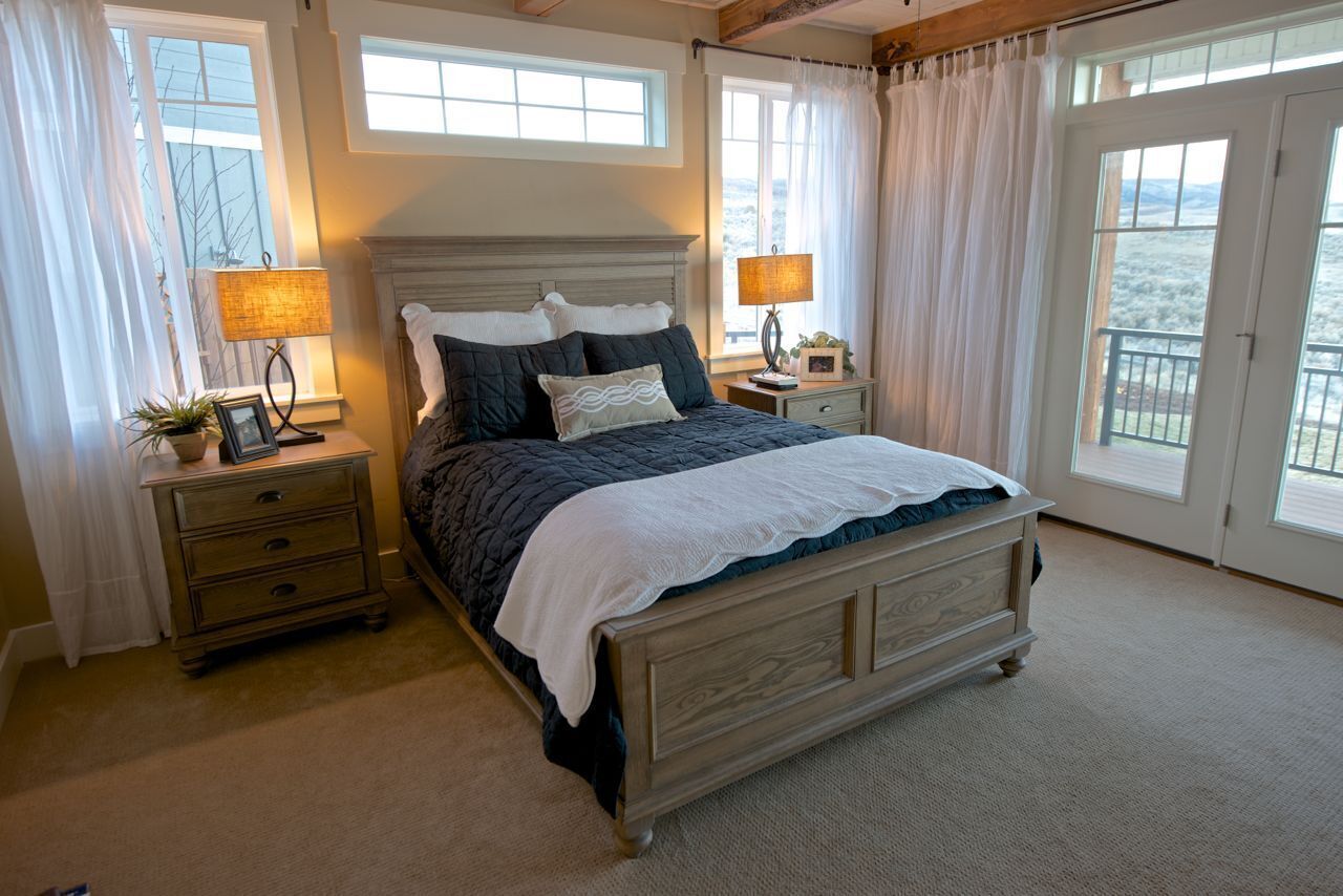 A bedroom with a large bed, two bedside tables, a nightstand, and a view of the outdoors through large windows.