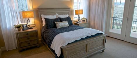 A bedroom with a large bed, two bedside tables, a nightstand, and a view of the outdoors through large windows.