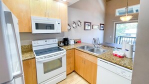 A compact kitchen with wooden cabinets, a microwave, stove, sink, and dishwasher.
